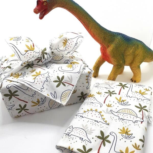 Un paquet cadeau en tissu écologique, Furoshiki, avec motif dinosaure. Parfait pour offrir à un petit garçon.