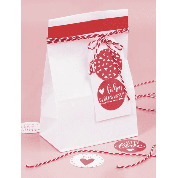 Un sachet en papier blanc personnalisé avec de la ficelle rouge et blanche et une étiquette cadeau.